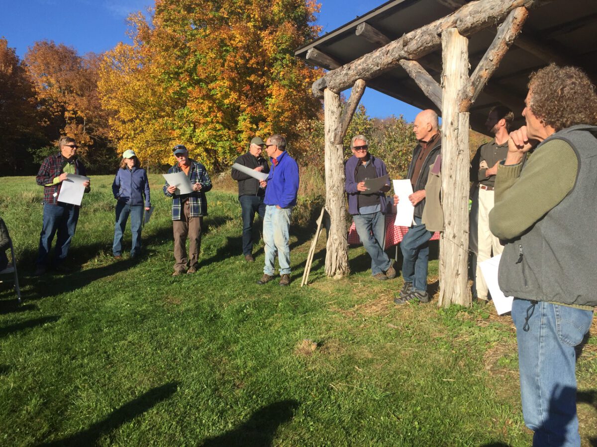 Group of people standing outside in sunshine, with autumn foliage visible behind them.