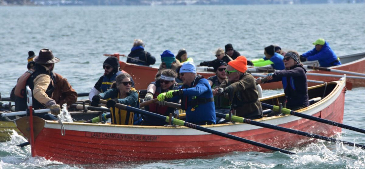 Three boats filled with rowers row on choppy water.
