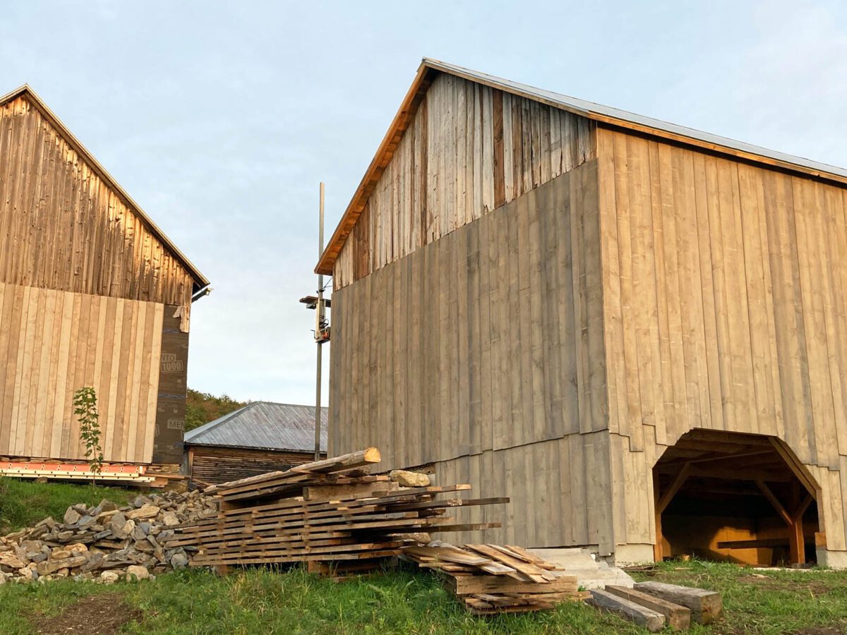 Timber frame barns with a pile of lumber in front.