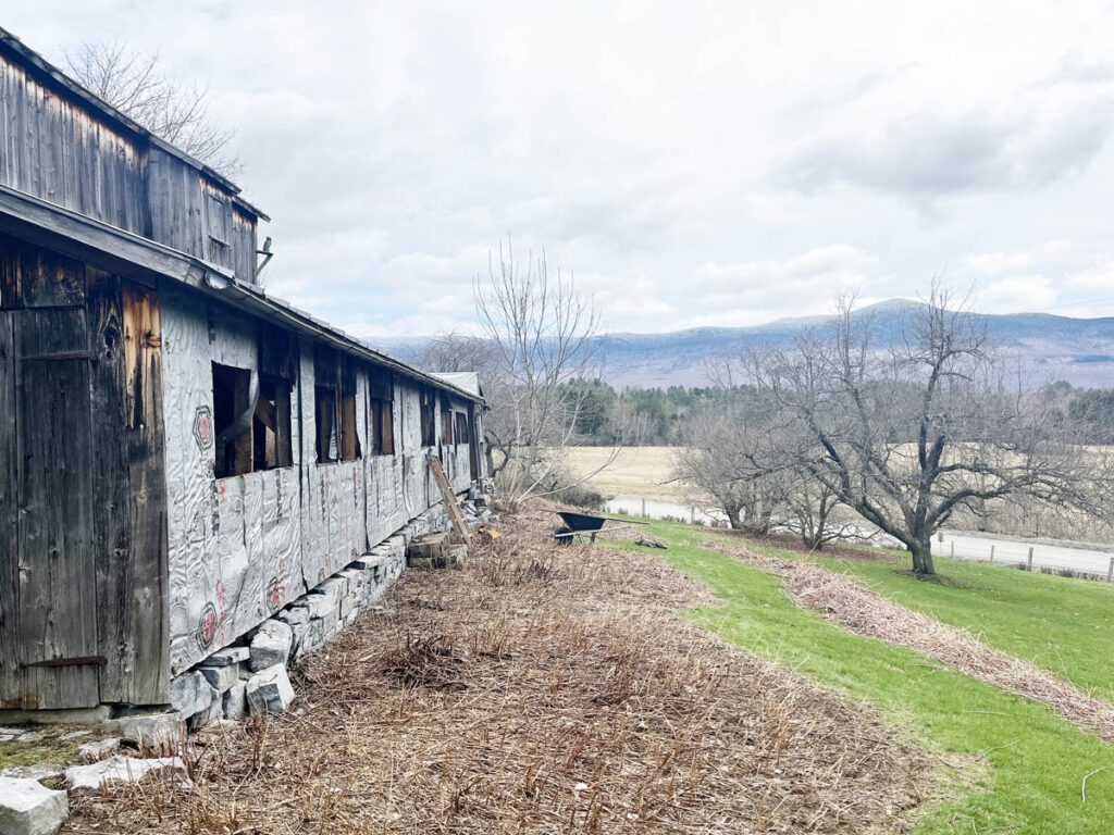 Side of an old barn, with mountains in the distance.
