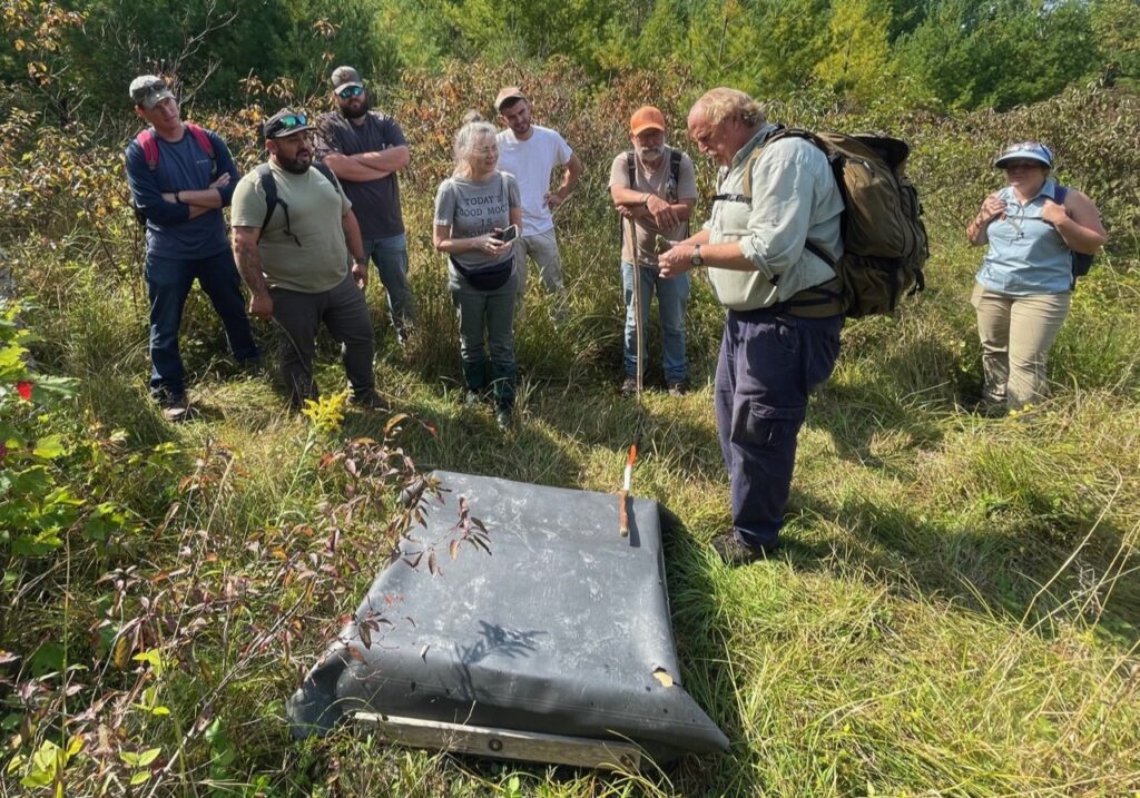 Researcher shows  snake to students in a meadow.
